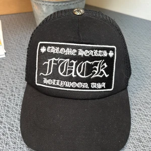 Svart keps från Chrome Hearts - Snygg svart keps från Chrome Hearts med texten 'F*** Hollywood USA' framtill. Kepsen har ett nätmaterial baktill och en justerbar rem för perfekt passform. Perfekt för en cool och avslappnad stil.