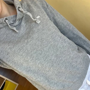 Grå hoodie från Lee - Säljer en grå hoodie från Lee i storlek XS. Den har en klassisk design med dragsko i huvan och ribbade muddar vid ärmslut och nederkant. Perfekt för en avslappnad stil.