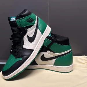 Air Jordan 1i grön och svart - Snygga Nike Air Jordans i en fräsch kombination av grönt, svart och vitt. Skorna har en klassisk hög design med snörning och den ikoniska Nike-loggan på sidan. Perfekta för dig som vill ha en stilren och sportig look.(®3ps)