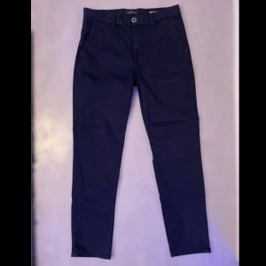 Svarta chinos från Hansen & Jacob - Snygga svarta chinos från Hansen & Jacob i storlek 32. Tillverkade av 96% bomull och 4% elastan för en bekväm passform. Klassisk design med knappar och bälteshällor, perfekt för en stilren look. Helt oanvänd dom har endast legat i garderoben och suttit där. Orginal pris 2099kr.