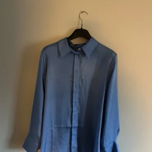 Blå långärmad skjorta - Snygg blå långärmad skjorta med klassisk krage och knappar framtill. Perfekt för en stilren look.