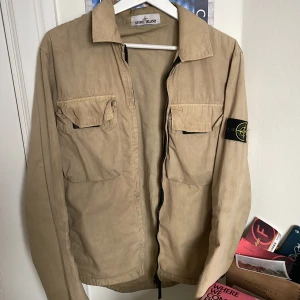 Stone Island Jacka/Overshirt - Säljer en snygg beige jacka från Stone Island med dragkedja. Jackan har en klassisk krage och den ikoniska Stone Island-loggan på ärmen. Perfekt för våren och sommaren!Skick 8/10 Kom dm för mer bilder eller frågor. Pris kan diskuteras