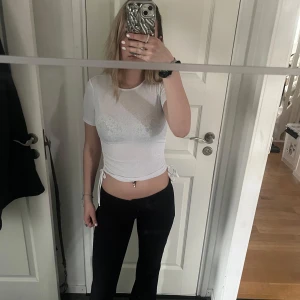 Vit ribbad kortärmad topp - Säljer en stilren vit ribbad topp med korta ärmar och knytning i sidorna. Perfekt för en avslappnad look eller att klä upp med accessoarer. Passar bra till både jeans och kjol.