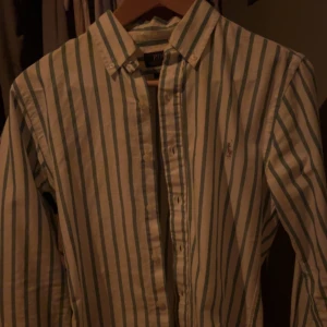 Randig skjorta från Polo Ralph Lauren - Snygg skjorta från Polo Ralph Lauren med gröna och vita ränder. Skjortan har långa ärmar och knappar framtill. Köpt i Spanien. Säljer pga för liten. Nypris cirka 1100:-