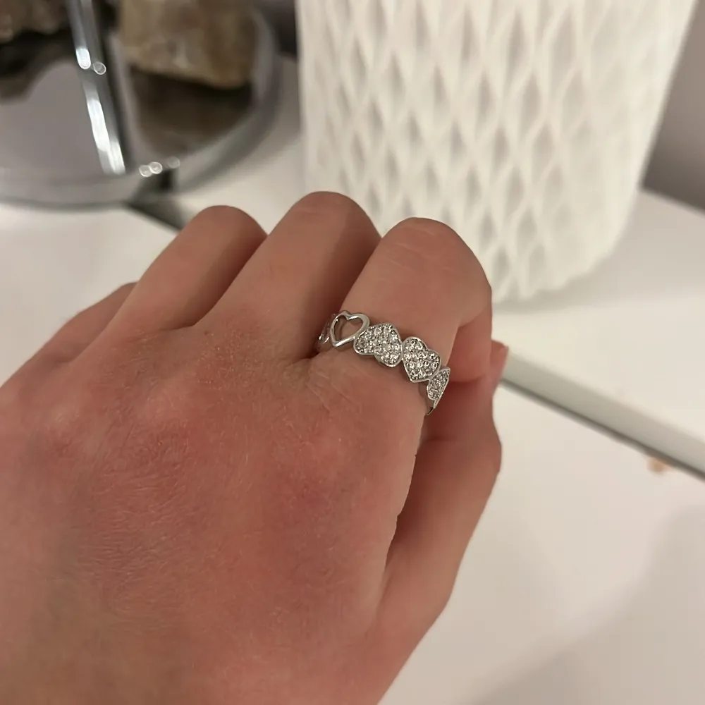 Elegant silverring dekorerad med glittrande stenar och hjärtformade detaljer. Perfekt för att ge en romantisk touch till din stil. Ringen har en fin glans och är designad för att passa bekvämt på fingret.. Asusteet.