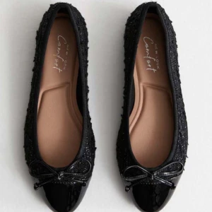 Svarta ballerinaskor från New Look - Snygga svarta ballerinaskor från New Look med glittrig yta och en söt rosett på tån. Perfekta för att ge en elegant touch till din outfit. Skorna har en bekväm passform och är lätta att bära hela dagen. Dem har varit använda 1 gång💗💗!köpta på Plick!