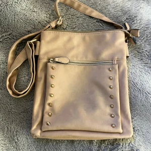 Beige axelväska med nitar - Snygg beige axelväska med justerbar axelrem och flera dragkedjefack. Väskan har en stilren design med nitar på framsidan och randigt foder inuti. Perfekt för att hålla ordning på dina saker med stil.