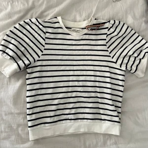 T-shirt tröja från Holly & Whyte - Säljer en stilren vit och marinblå/svart randig tröja från Holly & Whyte by Lindex. Tröjan har korta puff ärmar och en klassisk rund halsringning. Perfekt för en avslappnad och trendig look. Inget tecken på användning och pris kan diskuteras. Hör av dig vid intresse! 🖤
