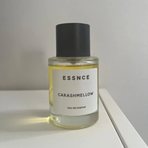 Essnce Carashmellow  - Säljer en flaska Essnce Carashmellow Eau de Parfum. Flaskan är rund med en svart kork och har en stilren etikett. Parfymen har en ljusgul färg och ger en känsla av elegans och sötma. Perfekt för den som älskar unika och mjuka dofter.