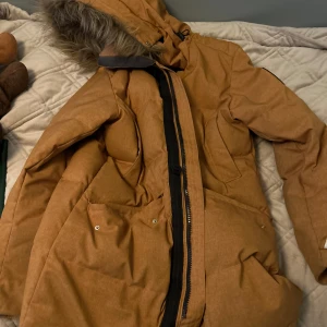 Senapsgul dunparkajacka från Helly Hansen - Säljer en dunjacka från Helly Hansen med pälskantad huva och dragkedja framtill. Jackan har långa ärmar och praktiska fickor. Perfekt för kyliga dagar. Nypris cirka 4000kr. 