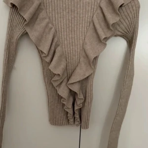 Beige ribbad tröja från Lindex - Säljer en beige ribbad tröja från Lindex med volangdetaljer längs framsidan.  