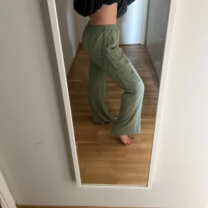 Gröna (tunna) cargopants med vida ben - Olivgröna byxor med resår i midjan. Byxorna har vida ben och fickor på sidorna - med band som går att knyta hur man vill/eller låta vara. Perfekt för utgång med klackar eller en avslappnad outfit