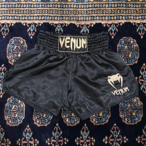 muay thai shorts - Säljer ett par svarta shorts från Venum med elastisk midja och guldlogga framtill. Perfekta för träning eller kampsport. 🥊