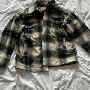 Rutig overshirt från Levi's - Snygg rutig overshirt från Levi's i gröna och svarta toner. Jackan har långa ärmar och knappar framtill samt två bröstfickor med knappstängning. Perfekt för lager-på-lager-stil. Nypris 1800kr