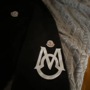 Svart tröja från Moncler - Säljer en svart tröja från Moncler med deras ikoniska logga på bröstet och ärmen. Tröjan har långa ärmar och en klassisk rund halsringning. Perfekt för en stilren look.