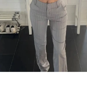 Grå randiga kostymbyxor från Bikbok i st 36 - Snygga grå kostymbyxor med vita ränder. Byxorna har en hög midja och en rak passform som ger en stilren look. Perfekta för en chic och professionell stil. Dom är knappt använda och har inga defekter!🥹🥹