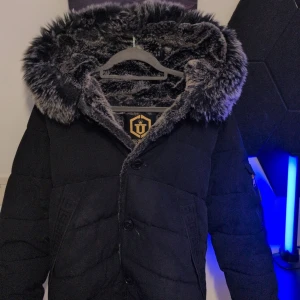 Svart jacka från Glorious Gangsta - Säljer en svart jacka främst som vinter jacka från Glorious Gangsta med en mysig fuskpälsfodrad huva. Jackan har dragkedja och knappar framtill samt en stilren design med märkets logga på ärmen. Perfekt för kalla dagar. Helt äkta päls. Päls över hela luvan som syns på bilden. Tvättas såklart innan och bara o skriva om de några frågor 😁