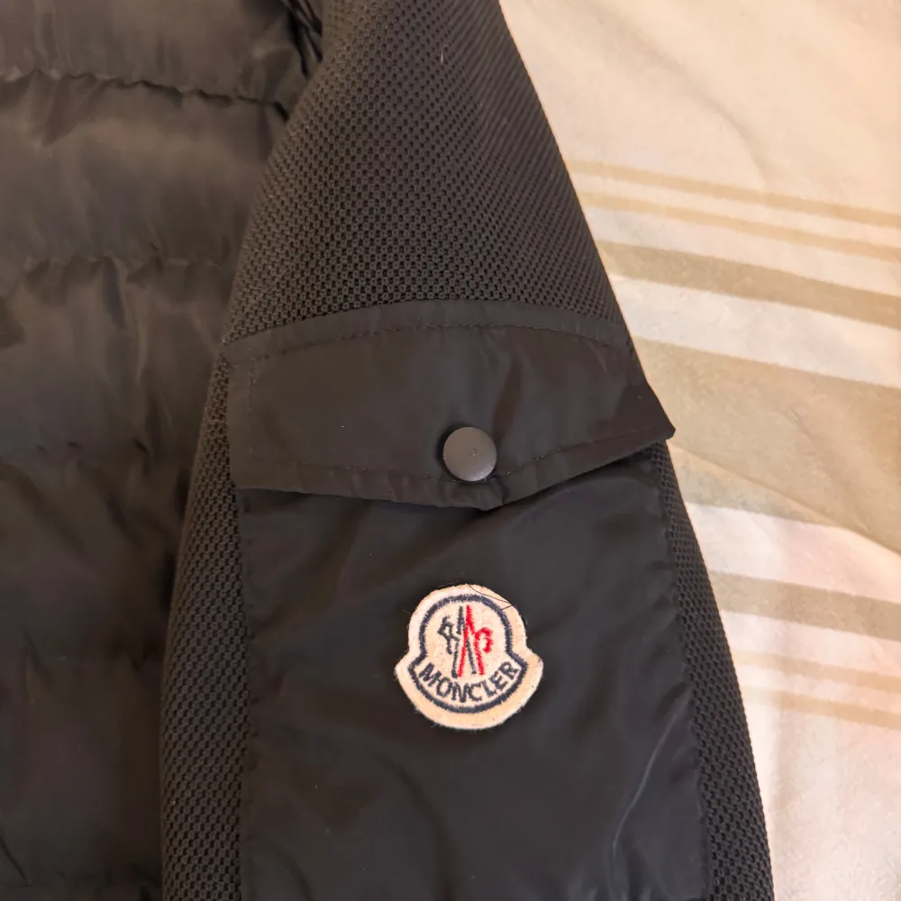 Snygg svart pufferjacka från Moncler med dragkedja och långa ärmar. Jackan har ett stilrent quiltat mönster och en broderad Moncler-logga på ärmen. Perfekt för kyligare dagar.. Takit.