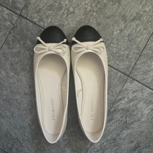 Ballerinaskor från Primark - Snygga ballerinaskor från Primark i beige med svart tå och en söt rosett framtill. Perfekta för en stilren look.
