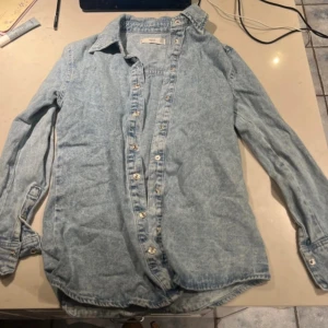 Ljusblå jeansskjorta från MNG - Säljer en snygg ljusblå jeansskjorta från MNG Denim. Skjortan har långa ärmar och knappar framtill. 