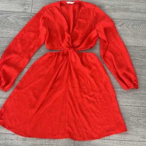 Röd klänning från H&M - Snygg röd klänning från H&M med långärmad design och knytning i midjan. Cut off i midjan Klänningen har en v-ringad stil och är perfekt för en färgstark look. Materialet är lätt och bekvämt.