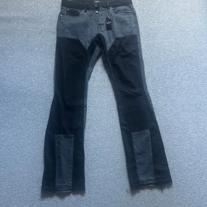Flared jeans från BoohooMAN - Unika byxor från BoohooMAN i svart och grått med kontrasterande paneler. Byxorna har en bootcut-stil och är perfekta för en trendig look. De har fickor både fram och bak samt en knappstängning.