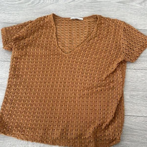 Brun spetsblus från Zara - Säljer en snygg brun spetsblus från Zara med korta ärmar och v-ringning. Perfekt för en stilren look. Blusen har ett vackert hålmönster som ger en luftig känsla. Passar utmärkt till både jeans och kjol. 🌟