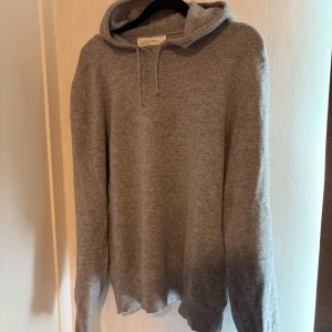 Grå kashmir hoodie från Sayless - Säljer en lyxig och mjuk grå hoodie i kashmir från Sayless. Perfekt för kyliga dagar med sin bekväma passform och stilrena design. Den har en klassisk huva med snörning och långa ärmar. Den är storlek L men passar M