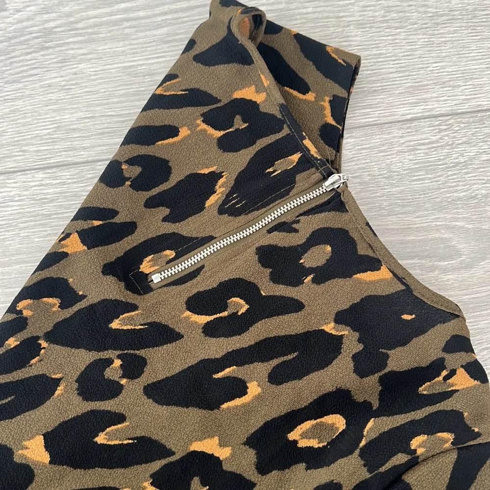 Snygg leopardmönstrad blus i jordnära färger med korta ärmar. Blusen har en praktisk dragkedja i ryggen för enkel på- och avtagning. Perfekt för att ge din outfit en vild touch!. Yläosat.