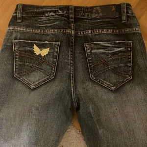 Jeans från Colours of the World - Snygga jeans i en klassisk blå tvätt från Colours of the World. De är mid/low waist och i modellen flare. Guldiga vingar på bakfickan!
