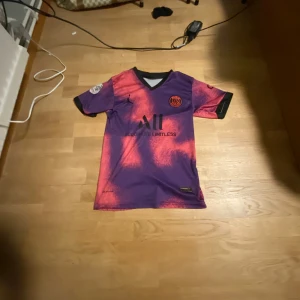 Lila och röd fotbollströja från Jordan - Snygg fotbollströja i lila och rött från Jordan med korta ärmar. Tröjan har ett unikt mönster och svart krage. Perfekt för fotbollsälskare som vill sticka ut på planen. 🔥