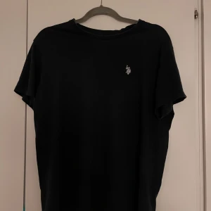Svart t-shirt från U.S. Polo Assn. - Säljer en klassisk svart t-shirt från U.S. Polo Assn. i 100% bomull. T-shirten har en liten broderad logga på bröstet och korta ärmar. Perfekt för en avslappnad stil.