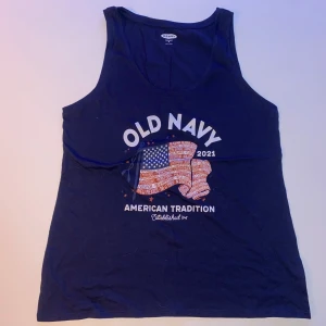 Mörkblå linnetopp från Old Navy - Säljer en mörkblå linnetopp från Old Navy med tryck av amerikansk flagga och texten 'American Tradition'. Perfekt för en avslappnad stil. 🌀