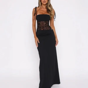 Svart långklänning med spetsdetalj - Supersnygg svart långklänning med smala axelband och transparent spets över midjan. Klänningen har en figurnära passform och raka linjer, perfekt för dig som vill sticka ut. Axelbanden är knytbara för extra detalj. Används i 3 timmar💕Säljs då jag inte kommer använda den något mer