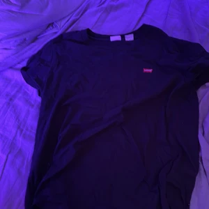 Svart t-shirt från Levi's, storlek L - En klassisk svart t-shirt från Levi's i storlek L. T-shirten har korta ärmar, rund halsringning och den ikoniska röda Levi's-loggan på bröstet. Tillverkad i mjuk bomull för en skön och avslappnad känsla. Typ helt ny inga defekter. Jag är 172 och den passar mig perfekt.
