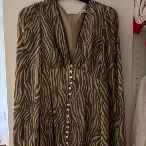 Zebramönstrad långklänning med knappar - Snygg trendig långklänning från Adoore!! Klänningen har långa ärmar, v-ringning och knappar hela vägen framtill. Klänningen har ballongärmar!! Använd en gång! Stl 36, lite svår i stl för de med större byst då den är lite tightare där. Det är även dragkedja i bak! 🤎🤎inköpspriset är 1695kr, därav säljer jag i högre pris. Men kom gärna med prisförslag!🙂