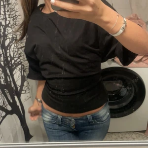 Svart omlottopp med knyt i ryggen - Säljer en svart POPULÄR TOPP FRPN NELLY  som knyts i ryggen. Toppen är croppad och har en cool, lite loose passform framtill. Perfekt för dig som vill ha något trendigt och unikt i garderoben., säljer då den inte kommer till användning 💞