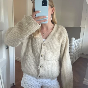 Beige stickad kofta med rosett - Supermysig beige stickad kofta med stora knappar och en söt rosettdetalj på ena fickan. Koftan har lång ärm, v-ringning och en lite loose passform. Perfekt att slänga på sig när det är kyligt ute. Populär Zara kofta med rosett som är beige från barnavdelningen men uppskattas som xs