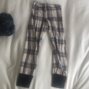 Rutig pyjamasbyxa från Calida - Mysiga rutiga pyjamasbyxor från Calida i vitt, blått och vinrött med breda svarta muddar vid bensluten. Byxorna har elastisk midja och är gjorda i mjuk bomull, perfekta för chillkvällar hemma.