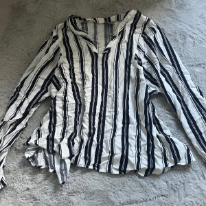 Randig långärmad skjorta från Lindex - Snygg långärmad blus från Lindex i vitt med svarta och mörkblå ränder. Skjortan har v-ringning. Nytt skick.