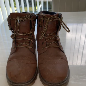 Bruna kängor från Livergy med rutigt foder - Stabila bruna kängor från Livergy med snörning och grov sula. Ovandel i skinnimitation och detaljer i mocka. Kragen har ett rutigt foder i blått och brunt som ger en snygg kontrast. Perfekta för höst och vinter när du vill ha både stil och funktion.