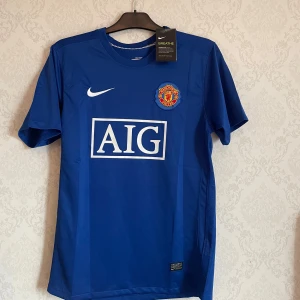 Manchester United Ronaldo 2007/2008 - Blå Manchester United fotbollströja från Nike med AIG som sponsor, klubbmärke på bröstet och Ronaldo 7-tryck på ryggen. Tillverkad i lätt och ventilerande material med korta ärmar och rund hals. Perfekt för dig som vill sticka ut på planen eller läktaren. Storlek M
