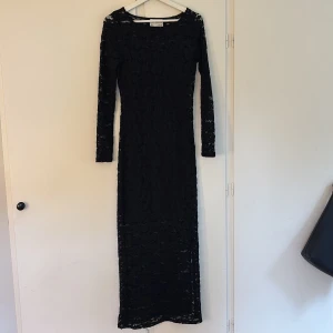 Svart långklänning i spets från Aware - Supersnygg svart långklänning från Aware med blommig spets och långärmad design. Klänningen har en figurnära passform och är helfodrad med transparenta ärmar. Perfekt för dig som vill sticka ut med en elegant och stilren look.