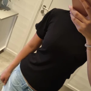 Svart ribbad t-shirt från KappAhl XS - En svart ribbad t-shirt från KappAhl i storlek XS. T-shirten har korta ärmar, rund halsringning och sitter snyggt figurnära. Perfekt till jeans eller kjol för en clean och enkel look.