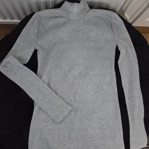 Grå ribbad polotröja med strass - Snygg grå ribbad polotröja med lång ärm och tight passform. Kragen är dekorerad med strassdetaljer som ger en extra touch. Perfekt för dig som gillar stilrena plagg med lite bling. Tröjan är i mjukt, stretchigt material och passar till många outfits.