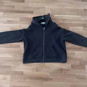 Svart hoodie med dragkedja Ruben Koné - Svart hoodie från Ruben Koné med hel dragkedja framtill och två stora fickor. Klassisk huva och långärmad modell i mjukt bomullstyg. Perfekt för chill dagar eller när du vill ha en enkel och stilren look. Pris går att diskuteras.