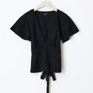 Svart omlottopp med knyt från Gina Tricot - Svart omlottopp från Gina Tricot med djup v-ringning, korta vida ärmar och knyt i midjan. Säljer för att den inte kommer till användning inga defekter. Bara att skriva om ni vill ha egna bilder💞