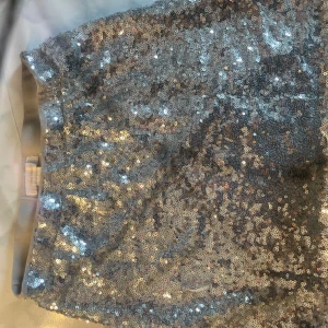 Glittrig silverkjol från Gina Tricot - Superglittrig kortkjol från Gina Tricot i silver med massor av paljetter över hela tyget. Kjolen har en rak passform och är fodrad på insidan för extra komfort. Perfekt för dig som vill sticka ut och glänsa.