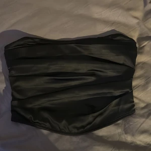 Svart satin tubtopp från ASOS DESIGN - Snygg svart tubtopp från ASOS DESIGN i glansigt satinliknande material. Toppen har en bandeauform och draperade detaljer framtill.