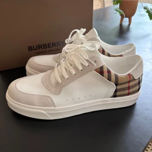 Burberry sneakers - Snygga sneakers från Burberry med klassiskt rutigt mönster på sidan, vita partier i skinn och mocka samt vita snören. Tjock vit sula och diskret Burberry-logga på plösen. Perfekta för dig som vill ha stilrena skor .